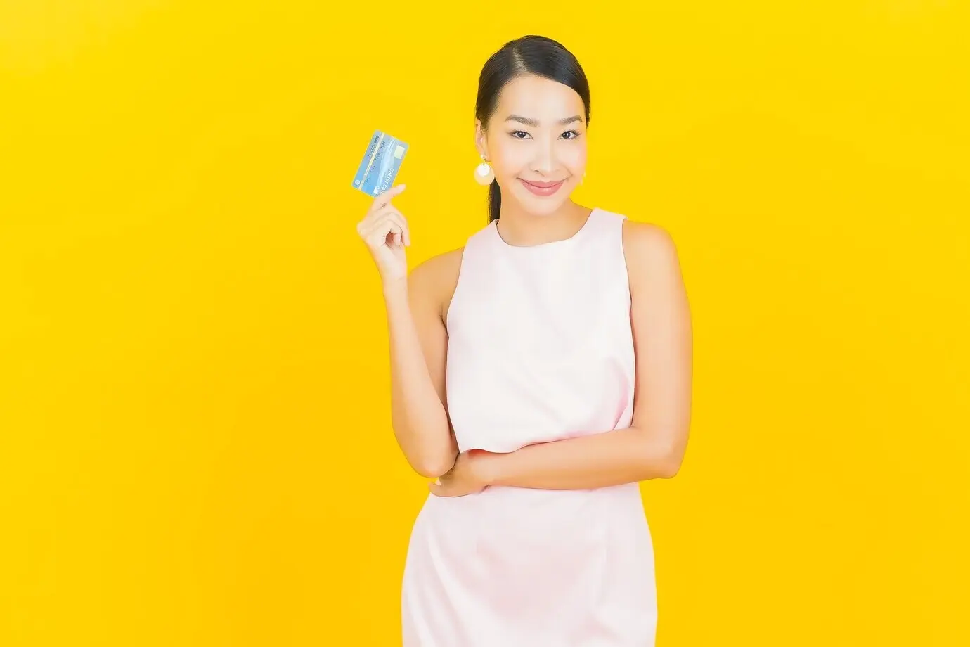 Portrait d’une belle jeune femme asiatique souriante avec une carte de crédit sur fond jaune.